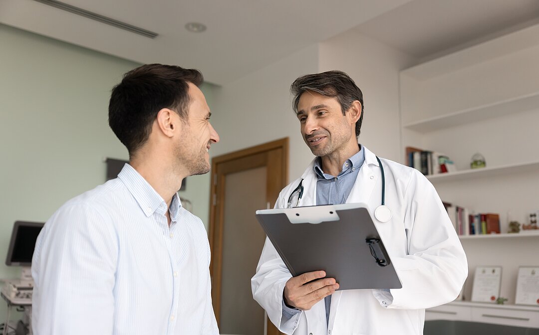 Doctor reviews information on a clipboard while speaking with a patient in a medical office.